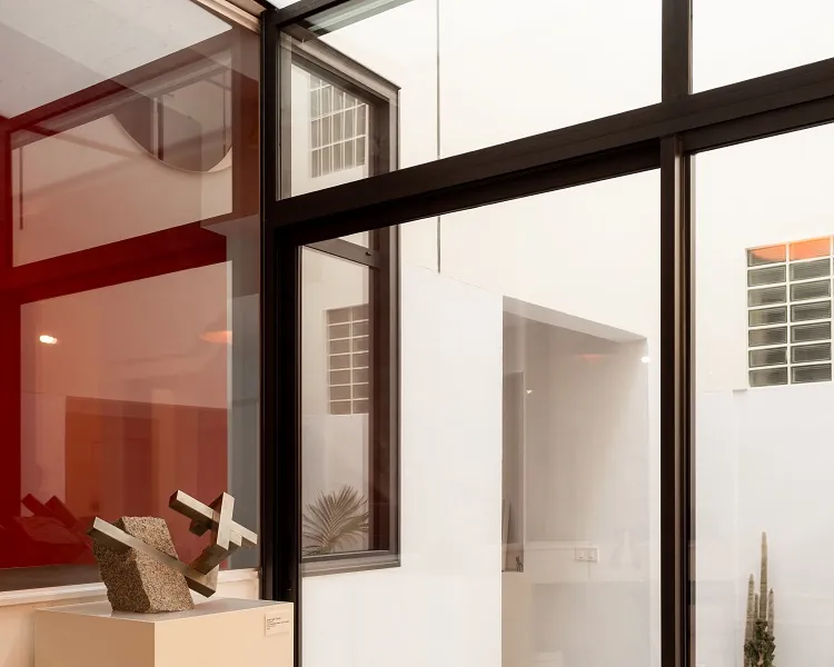 Fachada acristalada con perfilería de aluminio oscuro en patio interior